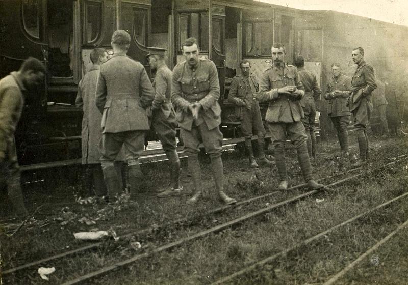 Journey to the front in France.jpeg - A meal break on the railway journey to the front in France. Names are: On extreme left: Captain Leeson, Captain Bellings (in Burberry, Captain Dowling (back to camera), Mr Belchie (Adjutant), Plum Warner (rubbing hands and facing camera), Captain Clay Mills (back to carriage door), Tom Preston (facing camera), Captain Goldie (back View), Captain Cane (facing), & Captain Dyer (hands in pockets)."